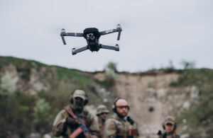 A drone taking off while people in camo watch.